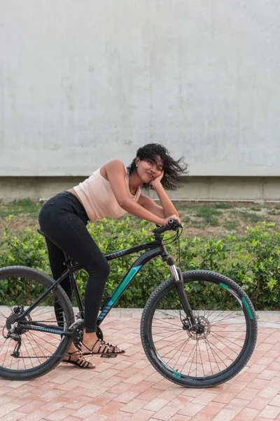 Yorgun genç bir kadın mola sırasında alnından ter silerken bisikletinin üzerinde dinleniyor..