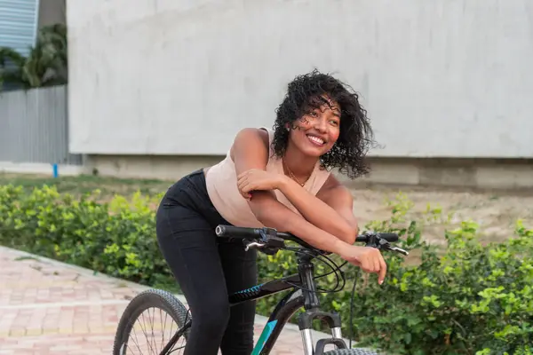 Neşeli, genç bir bisikletçi. Parlak bir gülümsemesi var. Bisikletine yaslanıyor..