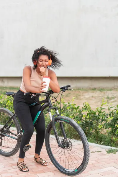 Bir kadın neşeli bir anı paylaşır, elinde kahveyle kıkırdar, bisikletine yaslanır..