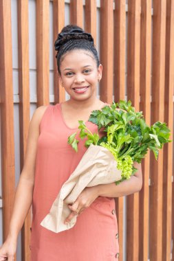 Kağıt torbada maydanoz tutan neşeli genç bayan..