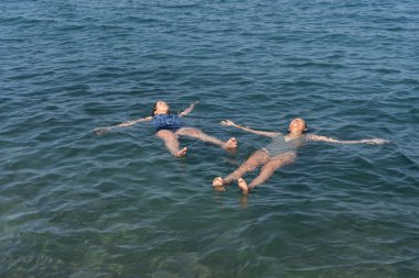 Sakin okyanusta iki insan sırtüstü yüzer, rahatlama somutlaşır..