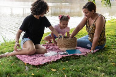 Bir aile piknikten zevk alır, göl kenarında bir sepet yemeği paylaşır..