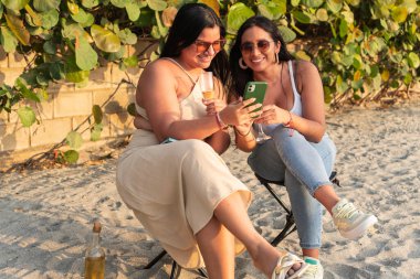 İki arkadaş gülüyor ve sahilde akıllı bir telefona bakıyor..