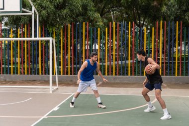 Dışarıda basketbol oynayan iki adam. Biri top sürüyor, diğeri savunuyor..