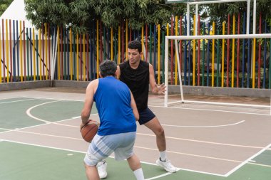 Açık hava sahasında bir basketbol maçında savunma ve hücum oynayan iki adam..