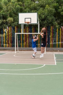 Siyah formalı bir adam dışarıda savunulurken basketbol oynuyor..