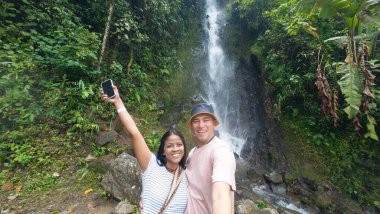 Zengin bir şelalenin önünde selfie çeken gülümseyen bir çift..