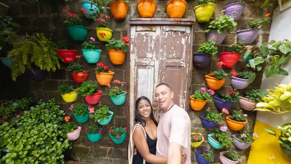 stock image Smiling couple posing in front of a vibrant wall decorated with colorful potted plants.