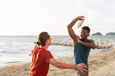 Okyanus kıyısındaki kumsalda frizbi oynayan iki atletik adam..