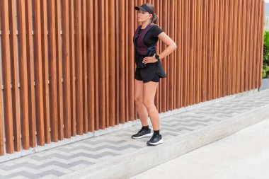 Koşuya ara veren bir kadın spor giyim mağazasında tahta bir çitin önünde duruyor..