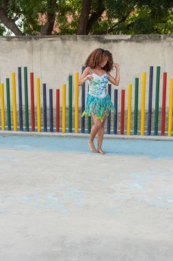Kıvırcık saçlı, neşeli püsküllü elbisesiyle dans eden genç bir kadın..
