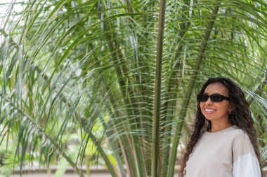 Tropikal bahçede gülümseyen güneş gözlüğü takan yerli kadın.