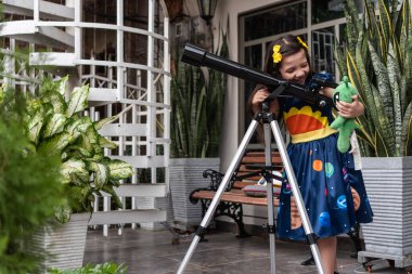 Girl Holding Alien Toy Next to Telescope Outdoors clipart