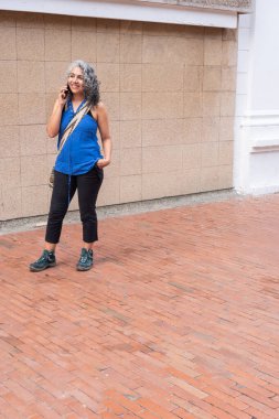 Tuğla kaldırımda telefonla konuşan gülümseyen kadın.