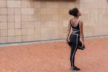 Şehirde koştuktan sonra bacaklarını açan genç ve sportif bir kadın.