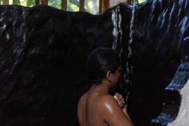 Woman washing in a basic outdoor shower in a rural area, enjoying a refreshing moment clipart