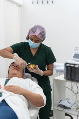 Güzellik uzmanı profesyonel güzellik kliniğindeki bir müşteriye altın maskeli tedavi uyguluyor.