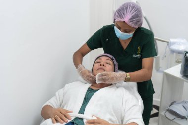 Latin Amerikalı güzellik uzmanı bir güzellik salonunda müşterinin yüzüne ve boynuna masaj yapıyor.