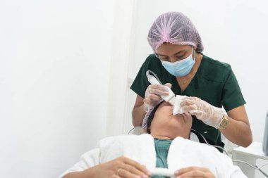 Güzellik uzmanı kadın hastada yüz temizleme için ultrasonik temizleyici kullanıyor.