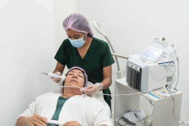 Latin güzellik uzmanı güzellik kliniğindeki bir müşteriye yüz bakımı için profesyonel bir güzellik aleti kullanıyor.