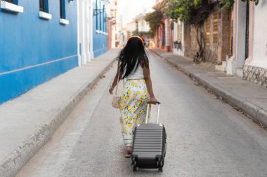 Kartagena, Kolombiya 'da renkli bir sokakta yürüyen genç bir turist bavulunu çekiyor.