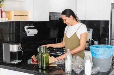 Mutfakta cam şişeleri, plastikleri ve kartonları ayıran kadın, sürdürülebilir bir yaşam tarzı için geri dönüşüm ve atık yönetimini teşvik ediyor
