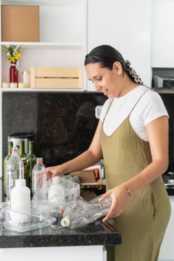 Latin bir kadın plastik şişe ve konteynırları torbaya koyup, geri dönüşüm ve atık ayrılığını teşvik ediyor.