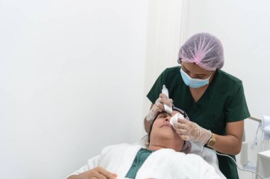 Profesyonel bir güzellik kliniğinde yüz bakımı sırasında müşterinin yüzüne ürün uygulayan bir güzellik uzmanı.