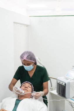 Güzellik uzmanı güzellik kliniğinde yüz bakımı sırasında ultrason makinesi kullanıyor.