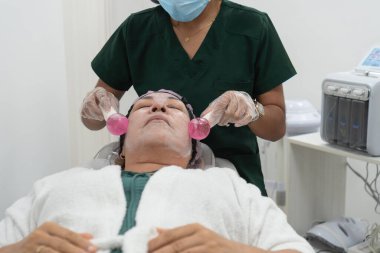 Güzellik uzmanı bir güzellik salonunda yüz bakımı sırasında bir hastanın yüzüne dondurma çubuklarıyla masaj yapıyor.