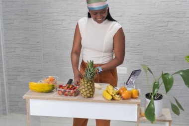 Gülümseyen etkili bir papaya, ananas, çilek ve muz tarifi hazırlıyor, akıllı telefondan video kaydediyor.