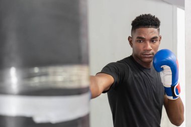 Genç boksör kum torbasında antrenman yapıyor, yumruklarını çalışıyor ve boks yeteneklerini geliştiriyor.