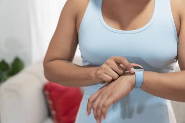 Açık mavi atletik bluz giyen bir kadın akıllı kasığıyla etkileşime giriyor, spor verilerini izliyor ve bağlantıda kalıyor.