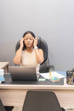 Stresli yönetici ofis masasında dizüstü bilgisayarla çalışırken kötü bir baş ağrısı çekiyor.