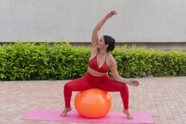 Turuncu fitness topunda pilates yapan kıvrımlı sporcu kadın vücut pozitifliğini ve sağlıklı yaşam tarzını destekliyor.