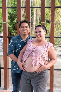 Mutlu İspanyol çift kucaklaşıyor ve hamile karnını dışarıda gösteriyor.