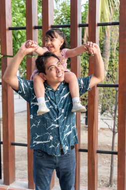 Mutlu İspanyol babası, gülümseyen kızını sırtında taşır ve parkta güzel vakit geçirir.