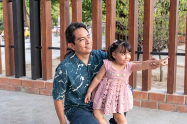 Aborjin İspanyol baba ve kızı tuğla bir duvar ve ahşap çitin yanında çömelmiş ve işaret ediyorlar.