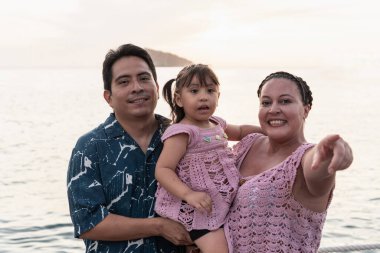 Mutlu İspanyol ailesi birlikte tatilin tadını çıkarıyor, gün batımında deniz kenarını işaret ediyor.