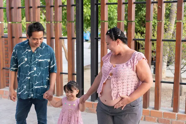 Mutlu İspanyol ailesi dışarıda eğleniyor. Hamile anne karnını ve kızının elini tutuyor.