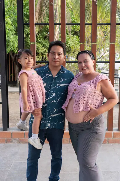 Mutlu İspanyol ailesi birlikte poz veriyor, hamile anne karnını tutuyor ve baba kızını kucağında tutuyor.