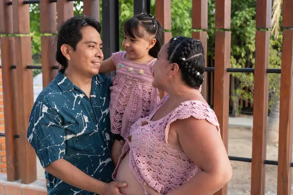 Mutlu İspanyol ailesi yeni bir bebek bekliyor, baba kızını kucağında tutuyor ve anne karnına dokunuyor.