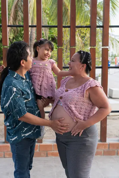 Mutlu İspanyol ailesi yeni bir bebek bekliyor, baba kızını kucaklarken anne karnını okşuyor.