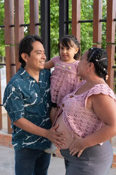 Mutlu İspanyol ailesi yeni bir bebek bekliyor, baba kızını kucağında tutuyor ve anne hamile.