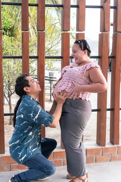 Mutlu İspanyol çift bebek bekliyor, koca şehir parkında hamile karnına dokunuyor.