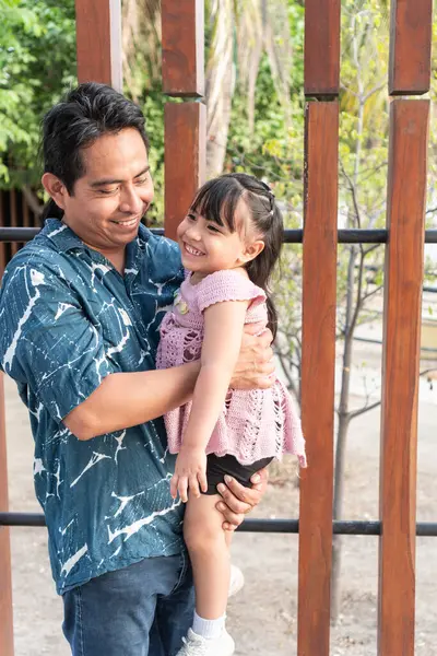 Mutlu İspanyol baba, neşeli küçük kızını kollarında tutuyor, birlikte güzel bir anın tadını çıkarıyor.