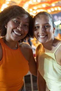 Canlı bir karnavalda iki arkadaş birlikte gülümsüyor.