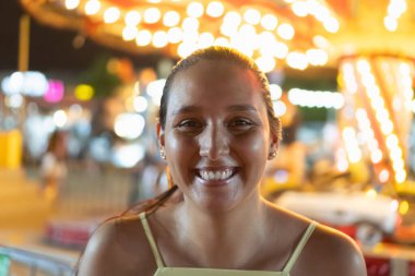 Arka planda renkli karnaval ışıklarıyla gülümseyen kadın.