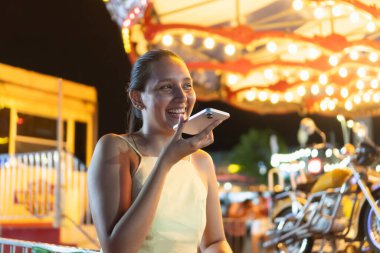 Canlı bir gece fuarında akıllı telefon kullanan gülümseyen kadın.
