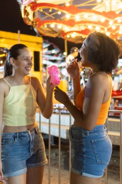 Canlı bir karnavalda gülen ve pamuk şeker yiyen iki kadın.